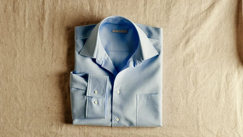 Hellblaues Oxfordhemd flach auf Leinen mit locker gerollten Ärmeln
