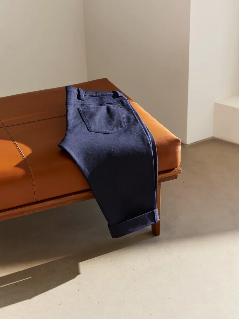 Marineblaue Chino über einer Holzbank mit Lederauflage in hellem Studio
